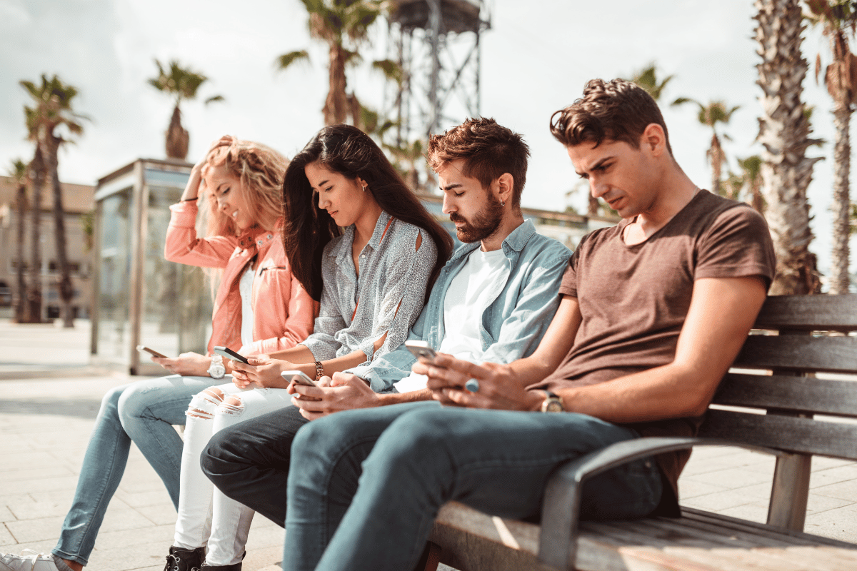 People on a bench looking down on phones - What if social media is the thing holding your coaching business back?